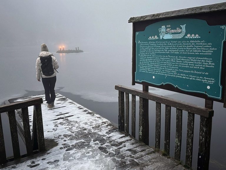 Das Bild zeigt den teilweise zugefrorenen Mummelsee im Schwarzwald. Auf dem Wasser schwimmt ein Abventskranz, an dem zwei Kerzen brennen.